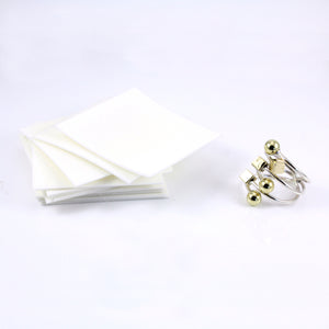 A stack of square jewelry polishing pads next to a clean,  shiny sterling silver and brass ring.